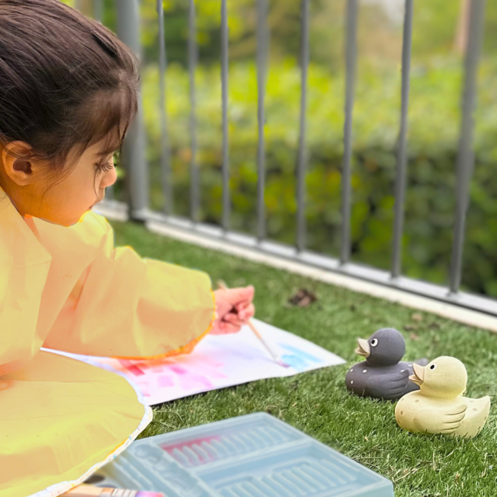 Lifestyle photo of child playing with natural rubber ducks outdoors. Mama & Bubba 